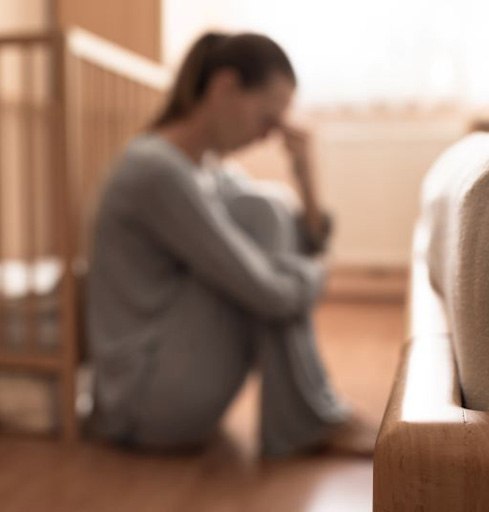 Crying woman sitting next to baby crib