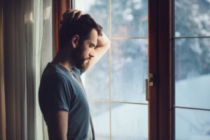 Depressed man standing at window during winter